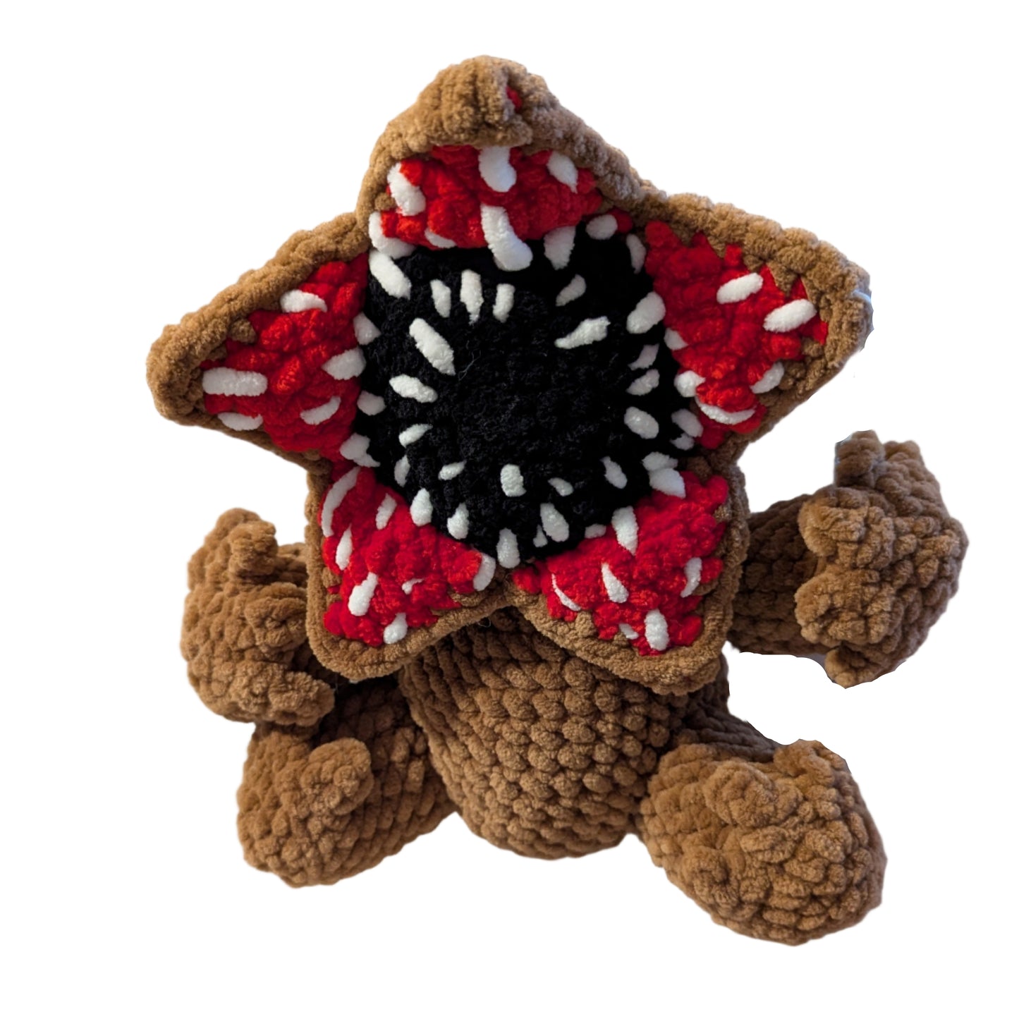 Crocheted creature with a red and black star-shaped head on a white surface.