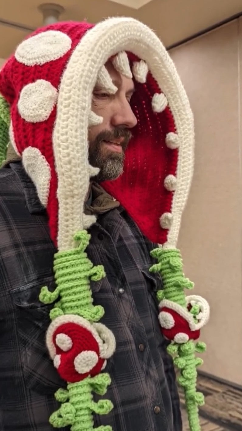Person wearing a red and white mushroom-shaped knitted hat and scarf.