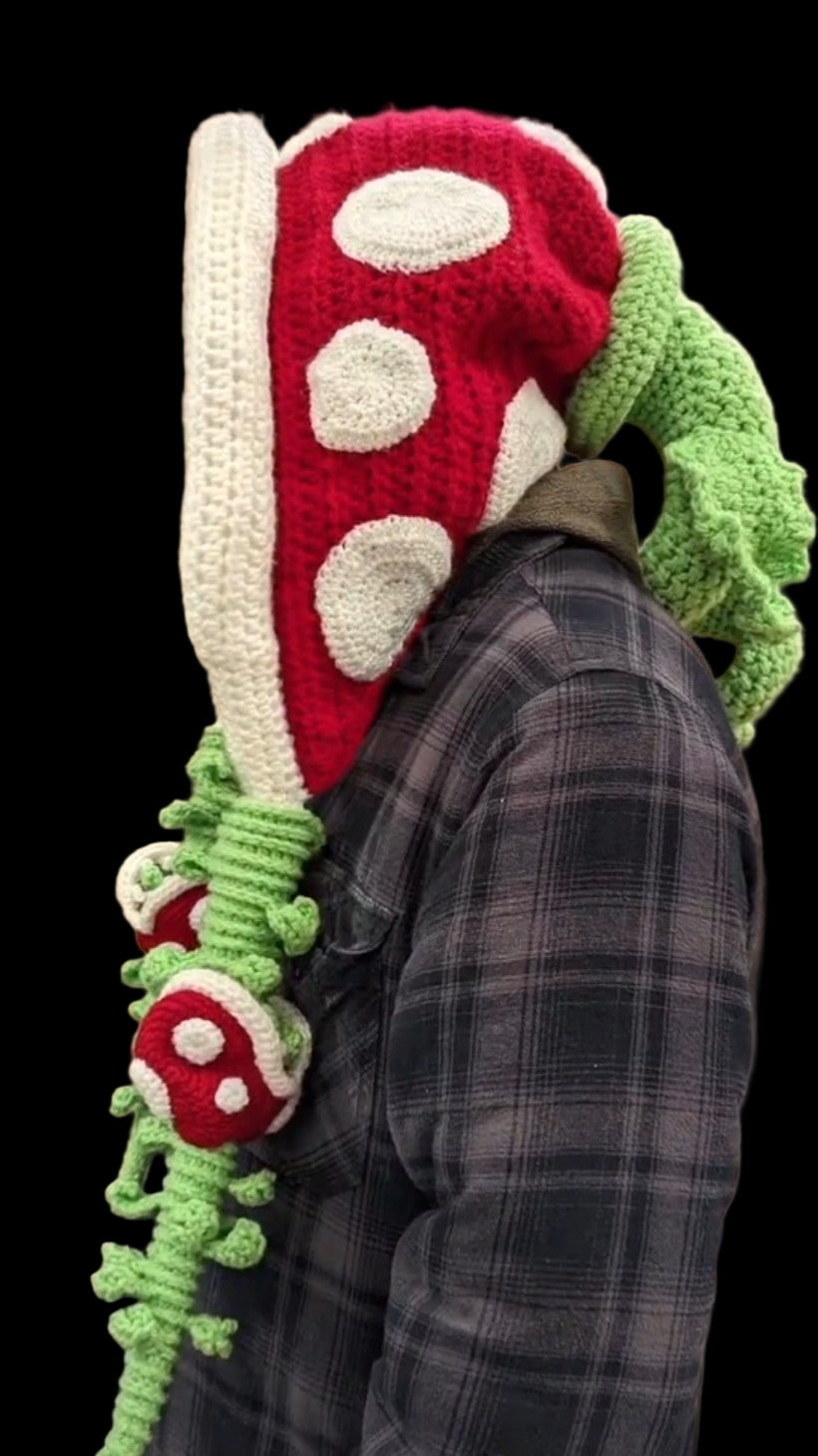 Person wearing a large, colorful knitted mushroom hat and scarf in an indoor setting.