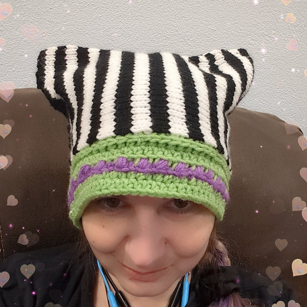 Person wearing a zebra-striped knitted hat with green trim against a heart-patterned background